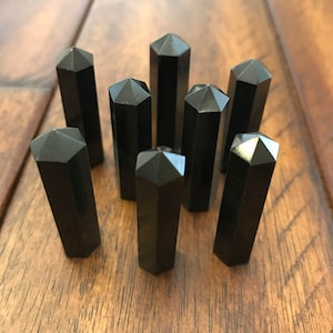 May include: Eight black obsidian crystal points arranged in a circle on a wooden surface.