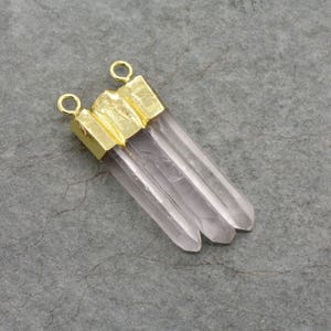 May include: A gold-plated pendant with three clear quartz crystal points. The pendant has two loops for attaching to a necklace or bracelet.