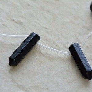 May include: Four black, pointed, gemstone beads strung on a clear cord. The beads are all the same size and shape.