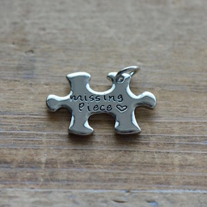 May include: Silver puzzle piece charm with the words "missing piece" and a small heart engraved on it.
