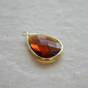 May include: A teardrop-shaped pendant with a gold-toned metal frame and a brown faceted glass stone.