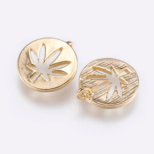 May include: Two gold-toned metal charms in the shape of a circle with a cut-out marijuana leaf design. One charm has a textured surface and the other has a smooth surface.