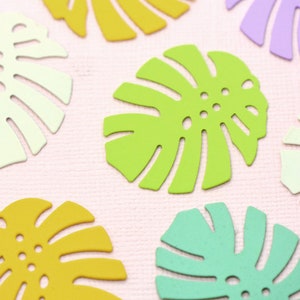 May include: Assortment of colorful paper cutouts in the shape of monstera leaves. The leaves are in shades of green, yellow, and purple.
