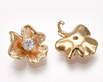 May include: Two gold-tone flower-shaped metal charms with a clear rhinestone in the centre. One charm has a loop on the top for attaching to a necklace or bracelet. The other charm has a hole in the centre for attaching to a string or chain.