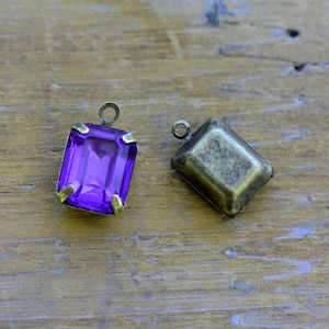 May include: Two metal settings for a pendant, one with a purple glass stone and one with a blank setting.