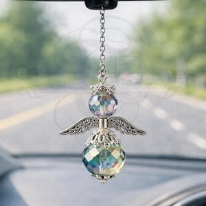 May include: A hanging car ornament featuring a silver-toned metal chain, a small crown-shaped topper, and two faceted iridescent crystal beads separated by a pair of detailed silver-toned metal wings, creating an angel-like silhouette.