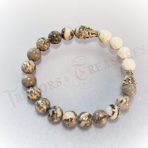 May include: A gray and white speckled stone bracelet with silver accents. The bracelet has a mix of round and oval beads.