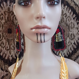 May include: A pair of beaded earrings with a lipstick design and gold feather accents. The earrings are black, red, and gold.