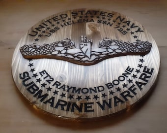 May include: A wooden plaque with a carved submarine emblem, the text "UNITED STATES NAVY", "USS HELENA SSN 725", "ET2 RAYMOND BOONE", and "SUBMARINE WARFARE".