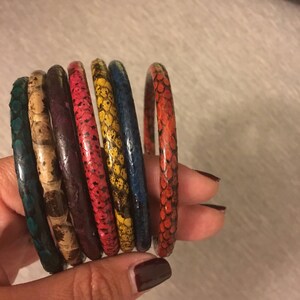 May include: A set of seven colorful snake skin bracelets. The bracelets are stacked on top of each other and are in the colors of teal, brown, purple, red, yellow, blue, and red.