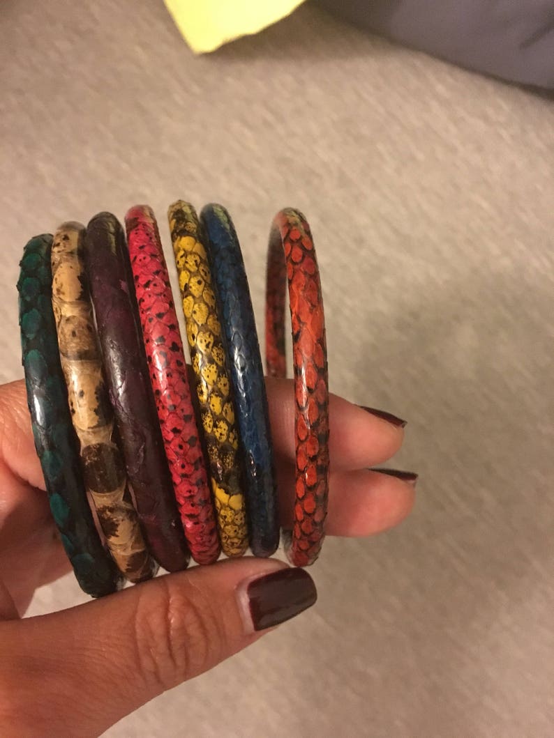May include: A set of seven colorful snake skin bracelets. The bracelets are stacked on top of each other and are in the colors of teal, brown, purple, red, yellow, blue, and red.