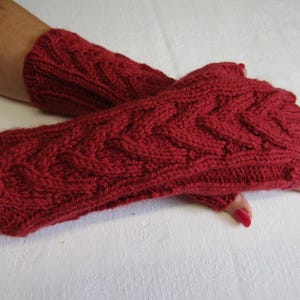 May include: Red knitted fingerless gloves with a cable knit pattern.