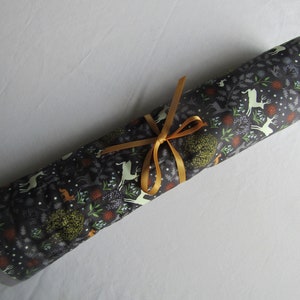 Puede incluir: Un rollo de tela gris con un estampado de ciervo blanco y bosque, atado con una cinta dorada.