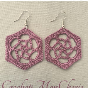 May include: A pair of mauve crocheted earrings with a hexagonal shape and a delicate floral design. The earrings have silver hooks.