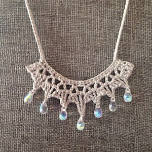 May include: A crocheted necklace with a delicate, lacy design and iridescent teardrop beads.
