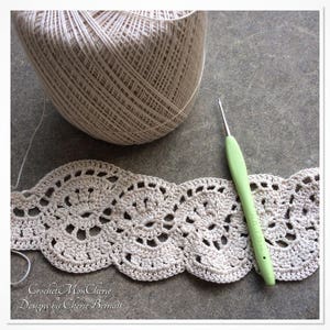 May include: A close-up of a crocheted lace trim in a cream color. A ball of yarn and a green crochet hook are also in the image. The text "Crochet Mon Cherie Designs by Cherie Bernatt" is visible in the bottom left corner.