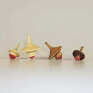 May include: Four wooden spinning tops with red tips. The tops are made of different types of wood and have varying sizes and shapes.