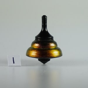 Op de afbeelding: Een zwarte en gouden draaitop met een puntige punt. De top heeft een gelaagd ontwerp met een zwarte basis en gouden accenten.