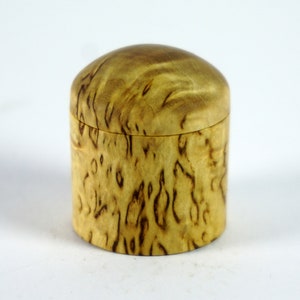May include: A small, round wooden box with a lid. The box is made of light wood with a dark brown swirl pattern.