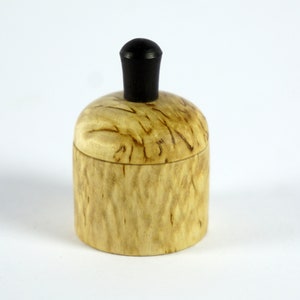 May include: A small wooden box with a natural wood grain finish and a black knob on the lid.