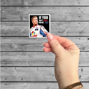 May include: A square sticker with a black background and a white border. The sticker features a photo of a race car driver wearing a racing suit and helmet. The text "IF YOU AINT FIRST YOU'RE LAST" is printed in white on the sticker.