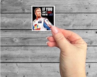 May include: A square sticker with a black background and a white border. The sticker features a photo of a race car driver wearing a racing suit and helmet. The text "IF YOU AINT FIRST YOU'RE LAST" is printed in white on the sticker.