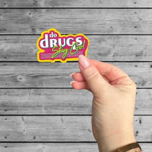 May include: A pink and yellow sticker with the text "do drugs stay cool" in a retro font.