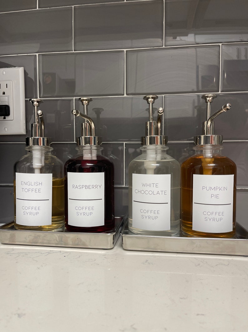 May include: Four glass bottles with silver pumps and labels. The labels read "English Toffee", "Raspberry", "White Chocolate", and "Pumpkin Pie". Each bottle has the text "Coffee Syrup" printed below the flavor.