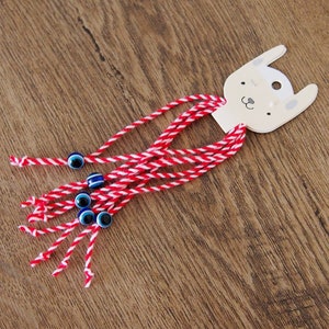 May include: A set of red and white string bracelets with blue evil eye charms attached to a white card with a cartoon bunny face.