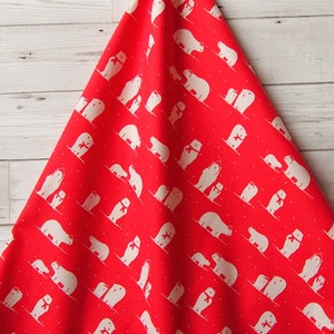 May include: A red kitchen towel with a repeating pattern of white polar bears wearing red scarves. The bears are depicted in various poses, some with their cubs, against a backdrop of small white dots. The towel is folded and hanging.