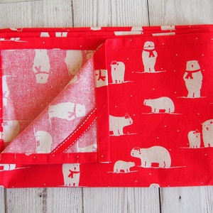 May include: Folded red fabric with a repeating pattern of white polar bears wearing scarves and hats. The fabric is folded to reveal a contrasting white interior with a red ribbon detail. The overall theme is winter or holiday.