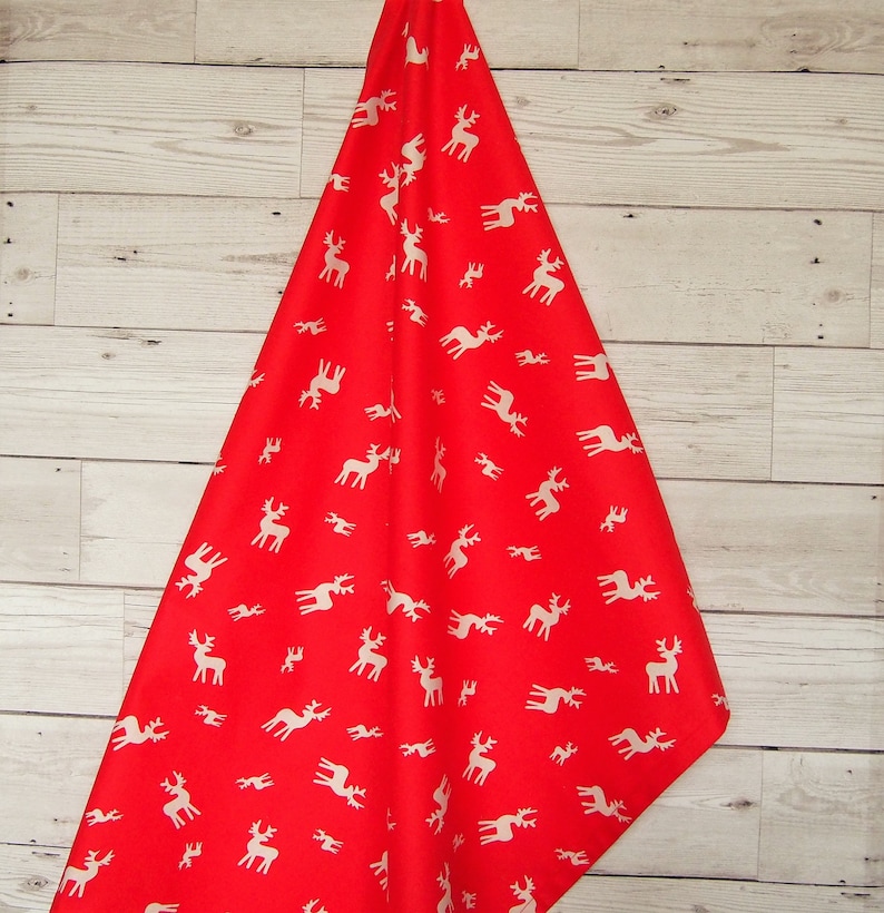 May include: Red fabric with a white reindeer pattern. The fabric is folded in a triangular shape.