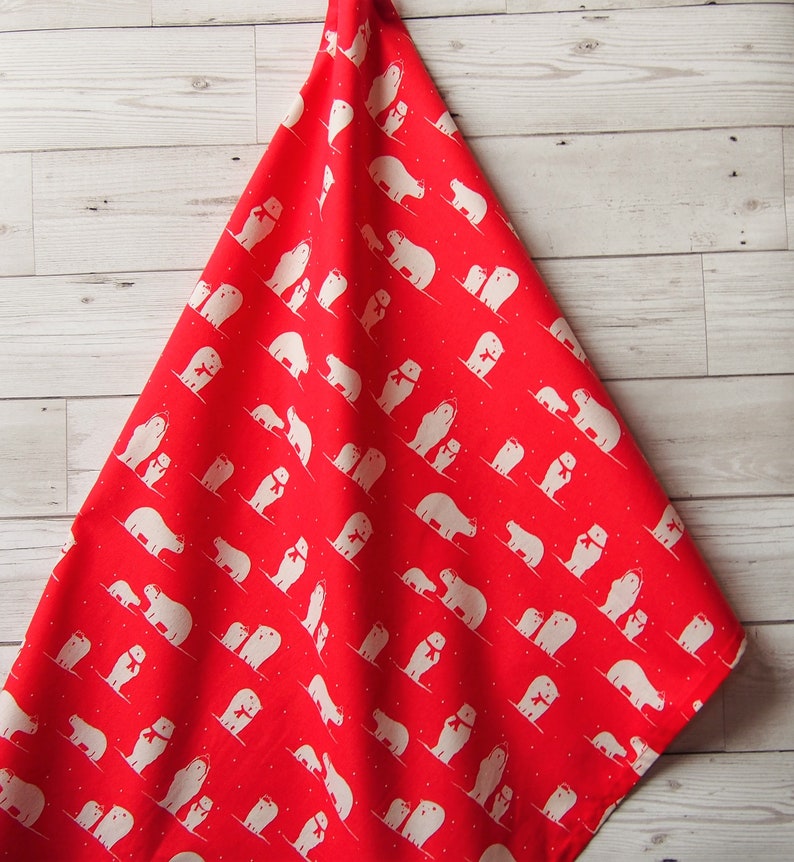 May include: A red kitchen towel with a repeating pattern of white polar bears wearing red scarves. The bears are depicted in various poses, some with their cubs, against a backdrop of small white dots. The towel is folded and hanging.