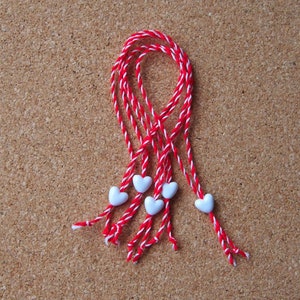 Op de afbeelding: Rood en wit touw met witte hartvormige kralen, gebonden in een lus.