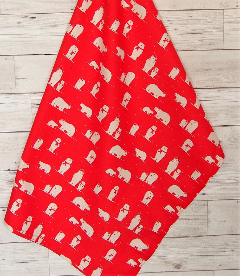 May include: Red fabric with a repeating pattern of white polar bears wearing red scarves. The bears are in various poses, some with their cubs. The fabric is hanging against a light wood background.