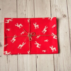 May include: A red gift box wrapped in paper with a white reindeer pattern and tied with twine.