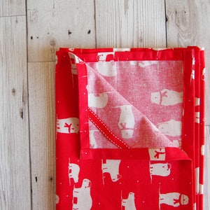 May include: Folded red and white patterned fabric, possibly a kitchen towel or napkin, with a repeating pattern of white polar bears wearing scarves. The fabric is folded neatly, with a portion of the interior pattern visible.