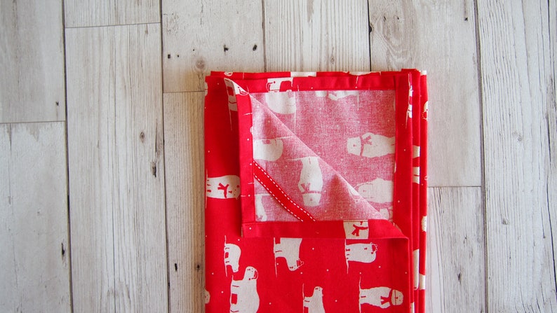 May include: Folded red and white patterned fabric, possibly a kitchen towel or napkin, with a repeating pattern of white polar bears wearing scarves. The fabric is folded neatly, with a portion of the interior pattern visible.