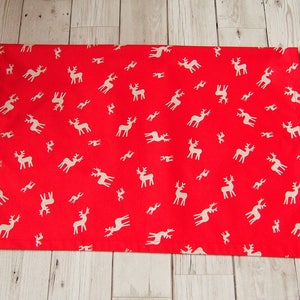 May include: Red fabric with a white reindeer pattern. The fabric is flat and appears to be a piece of wrapping paper.