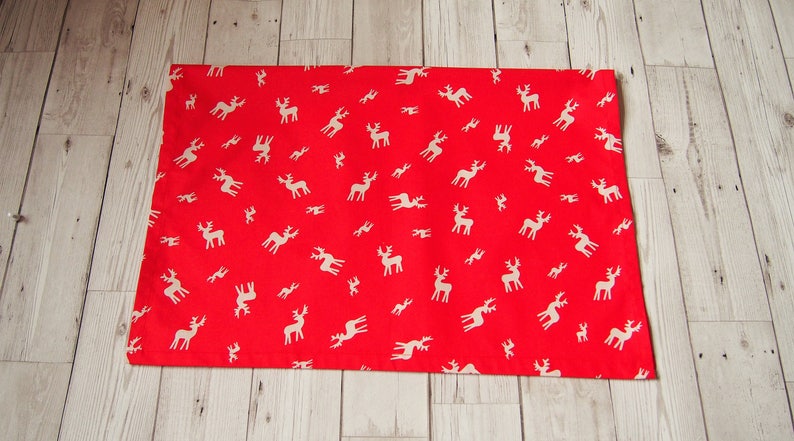 May include: Red fabric with a white reindeer pattern. The fabric is flat and appears to be a piece of wrapping paper.