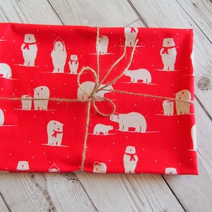 May include: A red fabric item wrapped with twine, featuring a repeating pattern of white polar bears wearing red scarves. The bears are in various poses, some with cubs. The fabric is folded and tied with natural twine.