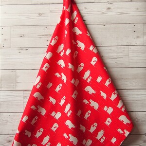 May include: A red fabric with a repeating pattern of white polar bears wearing scarves. The bears are in various poses, some with their cubs, against a backdrop of small white dots. The fabric is draped over a light wood surface.
