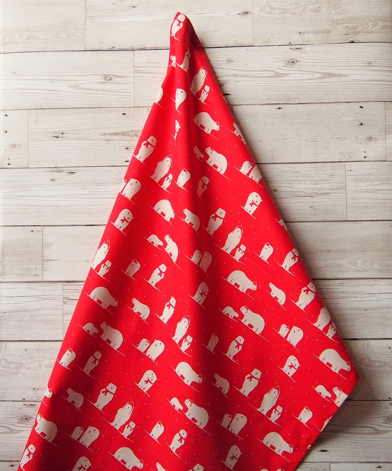 May include: A red fabric with a repeating pattern of white polar bears wearing scarves. The bears are in various poses, some with their cubs, against a backdrop of small white dots. The fabric is draped over a light wood surface.