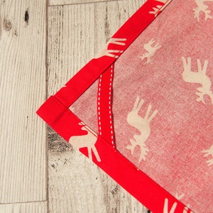 May include: A red fabric with a white reindeer pattern and a red border. The fabric is folded in a corner.