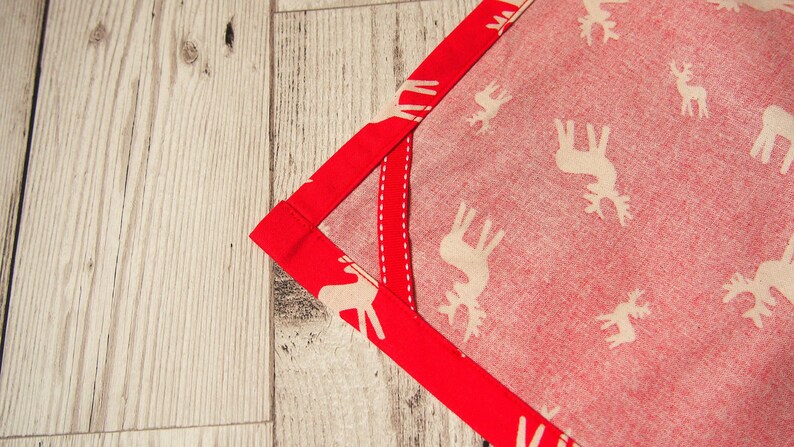 May include: A red fabric with a white reindeer pattern and a red border. The fabric is folded in a corner.