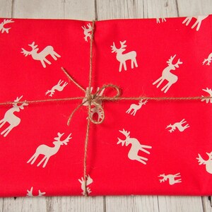 May include: Red wrapping paper with a white reindeer pattern. The paper is tied with twine.