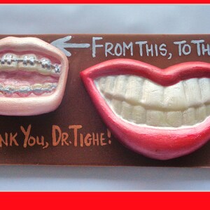 May include: A brown plaque featuring sculpted teeth, one set with braces, the other a perfect smile. Text reads "From This, To This!" and "Thank You, Dr. Tighe!"