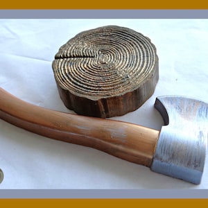 May include: A small, silver-painted axe with a wooden handle, and a wooden tree stump with concentric rings, both on a white surface.