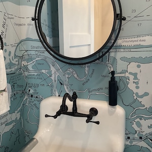 May include: A white porcelain bathroom sink with a black faucet and a black soap dispenser. The sink is in front of a wall covered in a nautical map wallpaper with blue and white colors. The map includes text like "Ocean Drive", "Whale Creek", "Burroughs Ho", "Corson Sound", "Thoro", "Strathm", "OTANK", "Chargeable Area", and "PON INLET".