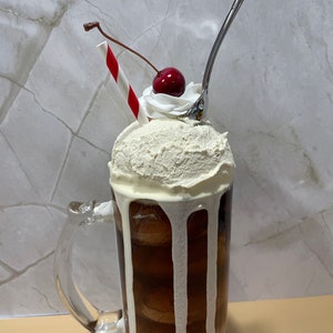 May include: A glass mug filled with a brown soda topped with vanilla ice cream, whipped cream, a red cherry, and a red and white striped straw.